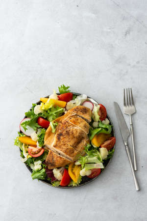 Delicious hearty lunch, chicken breast baked with spices and a mix of salad with tomatoes, radishes and cauliflower, top view, copy spaceの写真素材