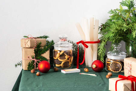 Festive decorated Christmas or New Year's table, thuja and spruce branches, candles and Christmas balls, chocolate chip cookies in a jar and gift boxesの写真素材