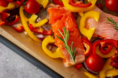 Baking sheet with cooked fish for baking, red fish Arctic char with tomatoes and peppers and rosemary on a baking sheet close-upの写真素材