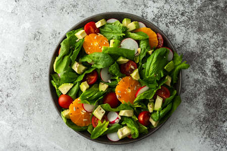 Delicious healthy salad of spinach leaves, tangerine and avocado slices, tomato and radish with seeds, salad in a plate close-up ,top view,copy spaceの写真素材