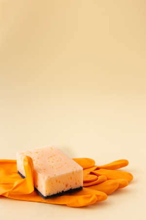 Orange dishwashing sponge and rubber gloves on neutral beige background, cleaning conceptの写真素材