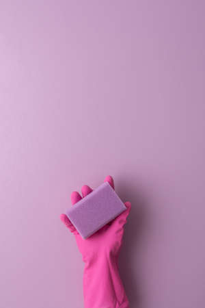 A hand in a pink protective rubber glove holds a washing sponge on a purple backgroundの写真素材