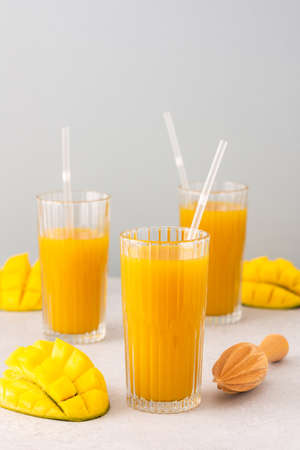 Freshly squeezed mango juice in glasses with a straw, ripe cut mango on a gray backgroundの写真素材