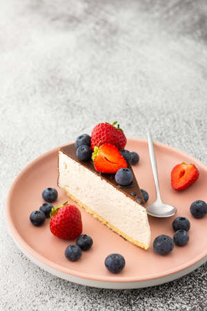 A piece of cheesecake covered with chocolate with blueberries and strawberries close-up on a pink plate with a dessert spoonの写真素材