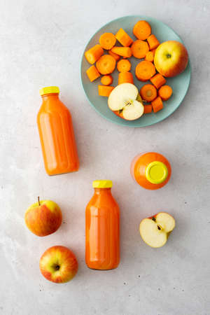 Carrot apple juice in bottles with fresh apples and carrots on a gray background, top viewの写真素材