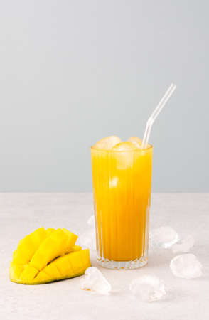 Freshly squeezed mango juice with ice in glass with a straw, ripe cut mango on a gray backgroundの写真素材