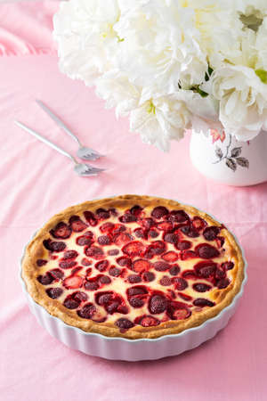 Table with a pink tablecloth, a bouquet of peonies and a sweet strawberry pie, a delicious summer dessertの写真素材