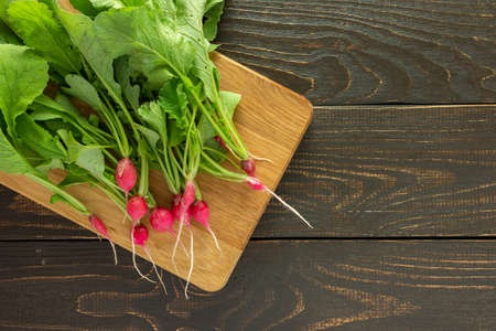 Freshly picked young radish with green tops on a board on a brown wooden background, organic products from the vegetable gardenの写真素材