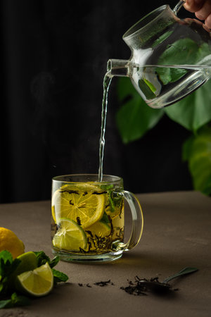 Woman pours boiling water from a teapot into a mug with mint, lemon, lime and black tea, tea brewing processの写真素材