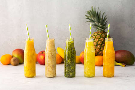 Fruit smoothies in jars with straws, in the background pineapple and kiwi fruits, banana and mango with orangeの写真素材