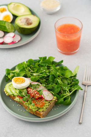 Healthy delicious breakfast, sandwich with avocado and salmon, cucumbers and radishes and microgreens of peas with boiled egg and corn salad, grapefruit smoothie in a glassの写真素材