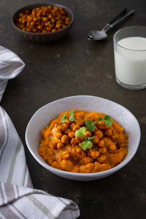 Thick pumpkin soup with baked chickpeas and radish sprouts in a plate with a glass of milk on the table, delicious healthy dinnerの写真素材