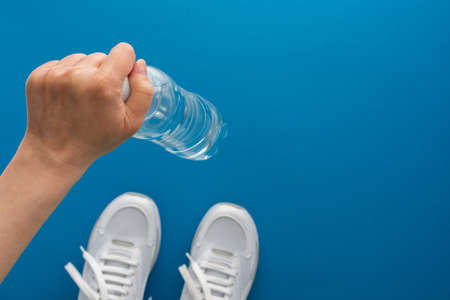 Female hand with a bottle of water, white sneakers on the floor, doing sports and training in the gym, active healthy lifestyle, top view, copy spaceの写真素材