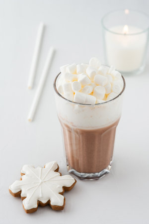 Glass with cocoa, milk froth and mashmellow, snowflake cookies, straws and a burning white candle, a delicious winter drinkの写真素材