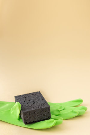 Black dishwashing sponge and green rubber gloves on neutral beige background, cleaning conceptの写真素材