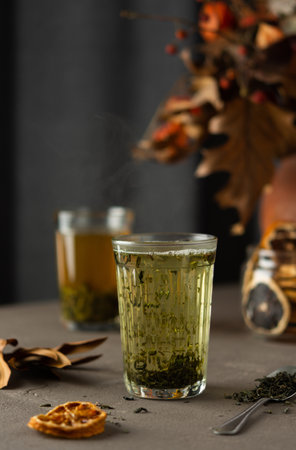 Glass of green tea against the background of an autumn bouquet and dry citrus fruitsの写真素材