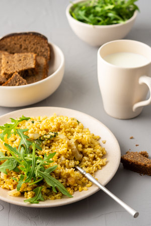 Delicious bulgur porridge with fried onions and herbs in a plate, a glass of milk, arugula in a bowl and black breadの写真素材