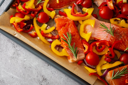 Baking sheet with cooked fish for baking, red fish Arctic char with tomatoes and peppers and rosemary on a baking sheet close-upの写真素材