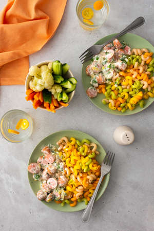 Colorful pasta with boiled sausages in sour cream sauce, fresh vegetables and boiled cauliflower, water with kumquatsの写真素材