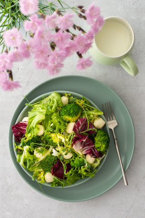 Top view of a table and a plate with light salad, green mix salad with broccoli, mozzarella cheese and microgreens, pink carnations in a vase a mug of milkの写真素材