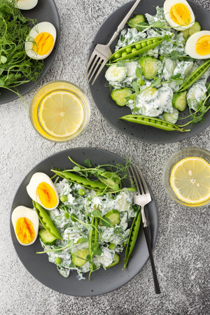 Salad with arugula, cucumbers and young peas with yogurt and boiled eggs with microgreens, lemon water in a glass, top viewの写真素材