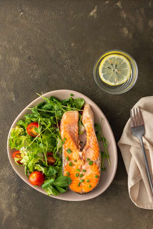 A delicious hearty lunch, a fried piece of trout steak and a mix of different types of greens salad, dinner with healthy red fishの写真素材