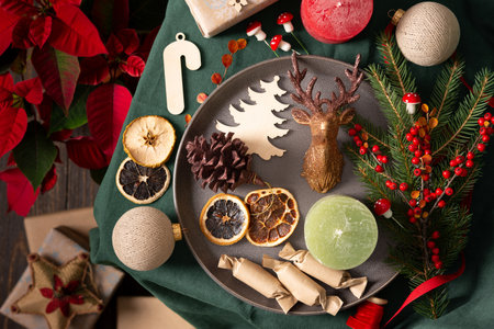 Christmas or new year background, balls and candy and candle, dried fruits and decorative deer , spruce and cotoneaster branches on a green tablecloth, poinsettia flower and gift boxes, top viewの写真素材