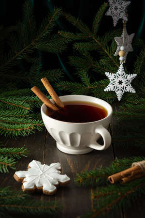 Ceramic mug with black tea and cinnamon among fir branches on a dark wooden background, delicious cookies in the form of a snowflake, Merry Christmas and Happy New Yearの写真素材