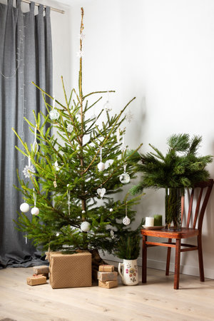Christmas tree with white toys, old chair with a vase with pine branches, gift boxes under the tree, part of home interiorの写真素材