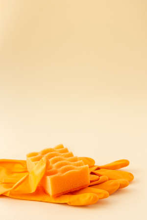 Orange dishwashing sponge and rubber gloves on neutral beige background, cleaning conceptの写真素材