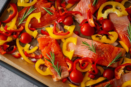 Baking sheet with cooked fish for baking, red fish Arctic char with tomatoes and peppers and rosemary on a baking sheet close-upの写真素材