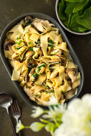 Fettuccini pasta with mushrooms and chicken breast and basil in a creamy sauce, top view, a vase of flowers on the tableの写真素材