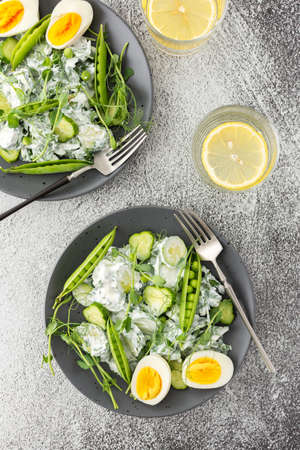 Salad with arugula, cucumbers and young peas with yogurt and boiled eggs with microgreens, lemon water in a glass, top viewの写真素材