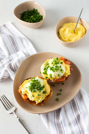 Delicious hearty breakfast, eggs Atlantic in a plate on a white background, round fried bun with salmon and eggs Benedict, hollandaise sauce and green onionsの写真素材