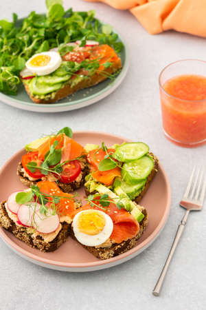 Healthy tasty breakfast, sandwiches with avocado and salmon, cucumbers and tomatoes, radishes and microgreens of peas with boiled egg and root salad, grapefruit smoothie in a glassの写真素材