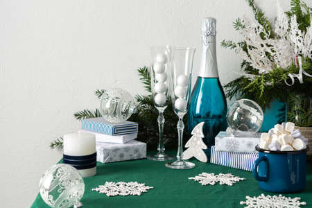 Festive decorated Christmas or New Year's table, thuja and decorative spruce branches, Christmas balls, a bottle of sparkling wine and glasses, a blue mug with marshmallows, gift boxes and snowflakesの写真素材