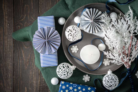 Christmas composition in white ,green and blue shades, christmas balls and candle, gift boxes and snowflakes, decorative white spruce branches and snowball on a green tablecloth, top view, copy spaceの写真素材