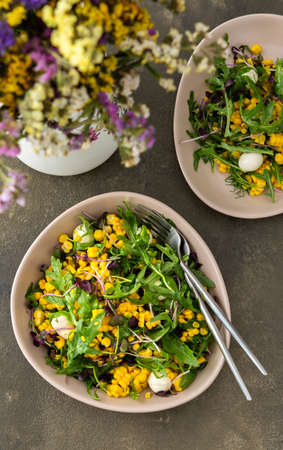 Salad with young boiled corn and mozzarella cheese, arugula and microgreen radish, fresh summer salad and flowers in a vase, top viewの写真素材