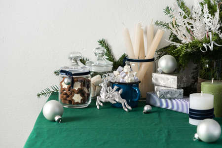 Festive decorated Christmas or New Year's table, thuja and decorative spruce branches, candles and gray balls, cookies in a jar and a blue iron mug with marshmallows, gift boxes and silver deerの写真素材