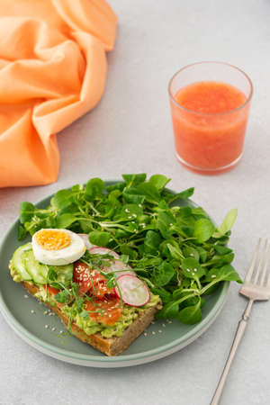 Healthy delicious breakfast, sandwich with avocado and salmon, cucumbers and radishes and microgreens of peas with boiled egg and corn salad, grapefruit smoothie in a glassの写真素材