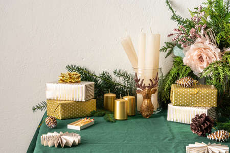 Festive decorated Christmas and New Years table, fir branches and decorative flowers, candles and golden gift boxes, Christmas tree decorations pine cones, deer and paper decorationsの写真素材