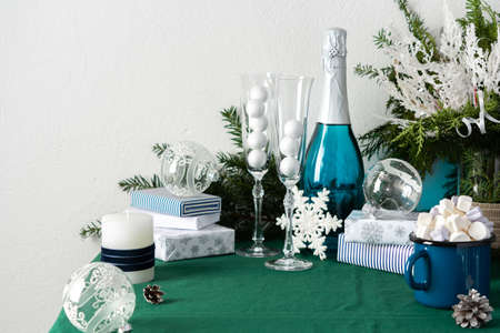 Festive decorated Christmas or New Year's table, thuja and decorative spruce branches, Christmas balls, a bottle of sparkling wine and crystal glasses, a blue iron mug with marshmallows, gift boxesの写真素材