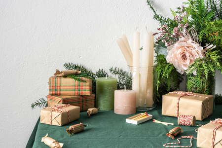 Festive decorated Christmas or New Year's table, thuja and spruce branches, candles and gift boxes, craft paper candies and decorative flowersの写真素材