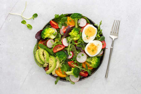 Delicious light breakfast, salad with tomatoes and radishes, avocado and boiled eggs, top viewの写真素材