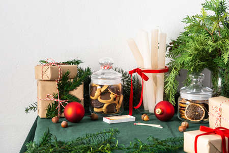 Festive decorated Christmas or New Years table, thuja and spruce branches, candles and Christmas balls, chocolate chip cookies in a jar and gift boxesの写真素材