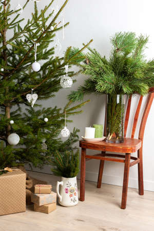 Christmas tree with white toys, old chair with a vase with pine branches, gift boxes under the tree, part of home interiorの写真素材
