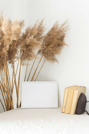 Home decor mock-up, blank picture frame near white painted concrete wall , dry Cane Reeds and old booksの写真素材