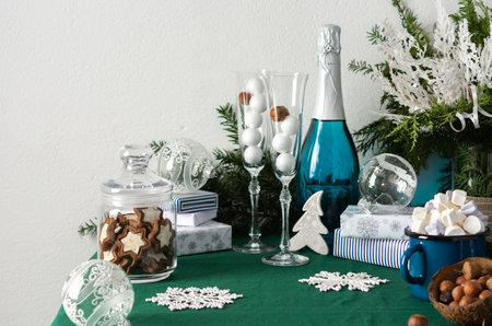 Festive decorated Christmas or New Years table, thuja and decorative spruce branches, Christmas balls, a bottle of sparkling wine and crystal glasses, a blue iron mug with marshmallows, gift boxesの写真素材