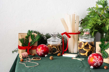 Festive decorated Christmas or New Years table, thuja and spruce branches, candles and Christmas balls, chocolate chip cookies in a jar and gift boxesの写真素材