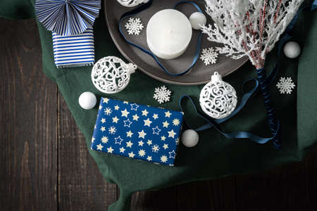 Christmas composition in white ,green and blue shades, christmas balls and candle, gift boxes and snowflakes, decorative white spruce branches and snowball on a green tablecloth, top view, copy spaceの写真素材